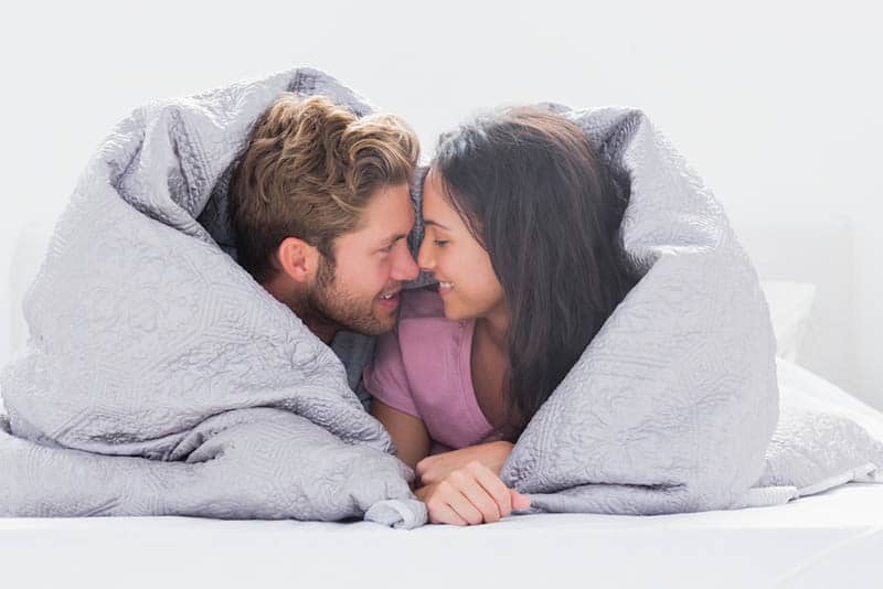couple in love lying on the bed wrapped into the blanket