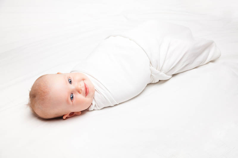 cute baby girl swaddled in white sheet lying on the bed