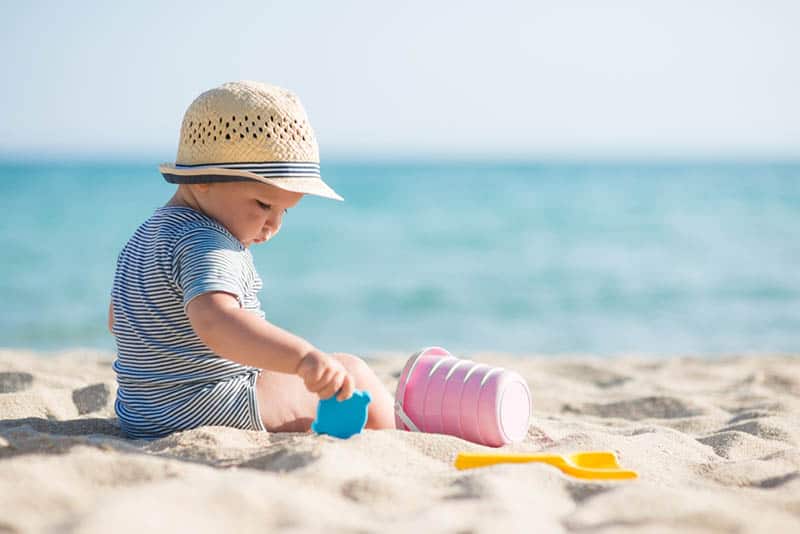 cute baby with hat playing in the sand on the beach
