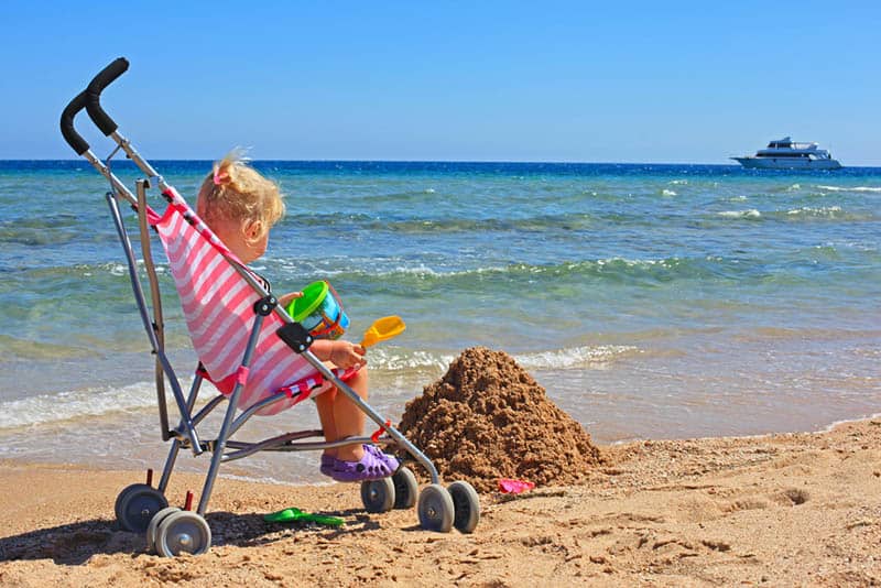 cute little girl playing in a stroller on the beach