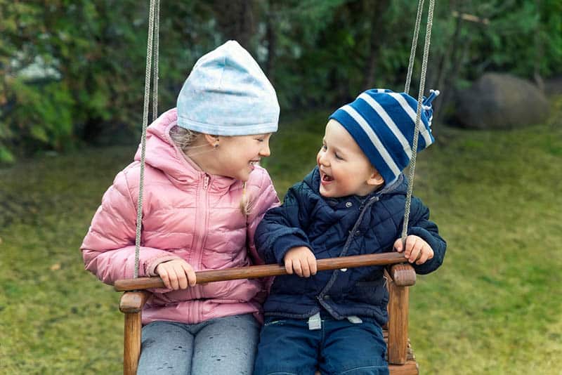 happy brother and sister swinging together in swingset