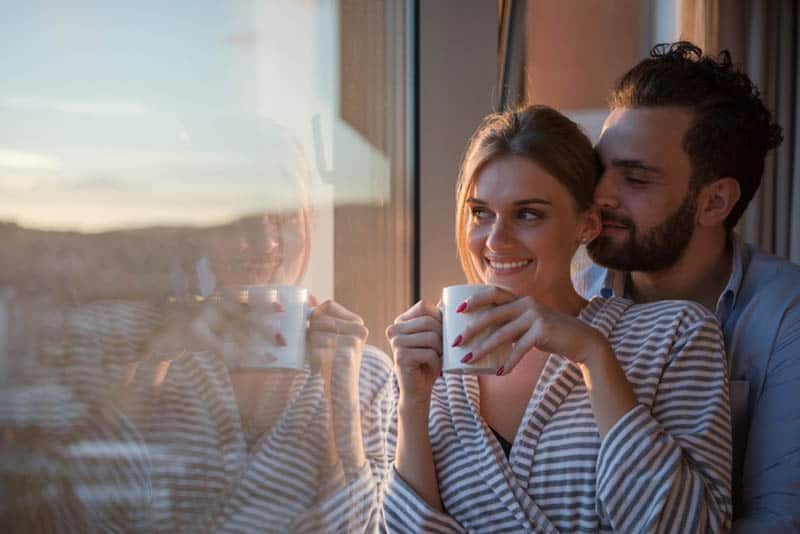 happy couple enjoying morning coffee by the window