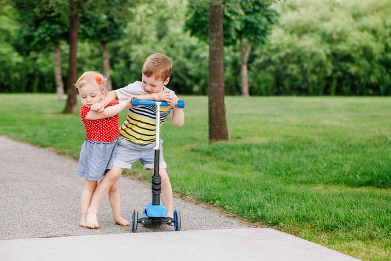 little boy pushing his sister from him in the park