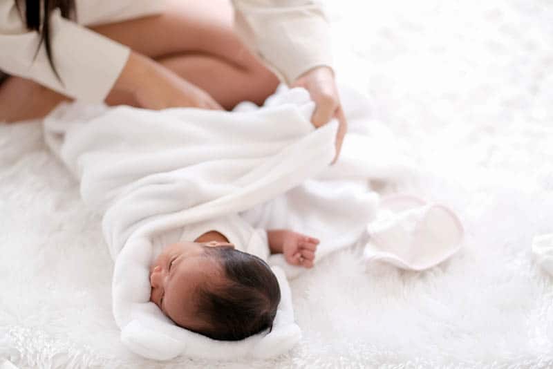 mother swaddling newborn baby with white cloth