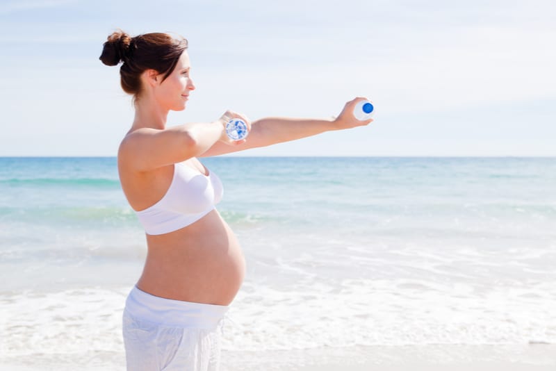 pregnant woman at the beach holding two water bottles