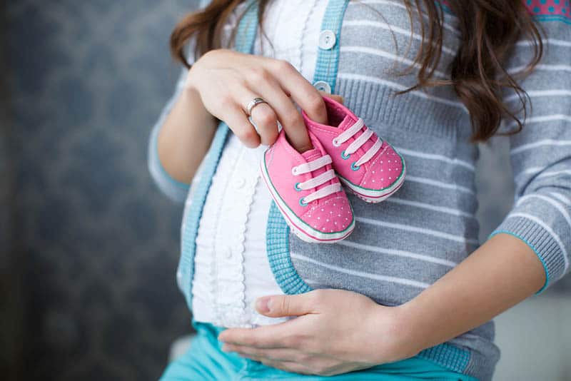 pregnant woman holding pink baby shoes