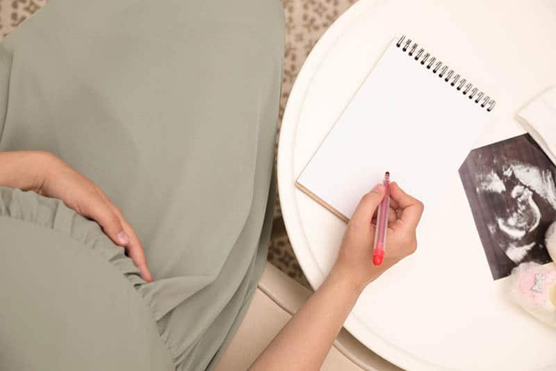 pregnant woman in dress writing on paper with sonogram picture on the table