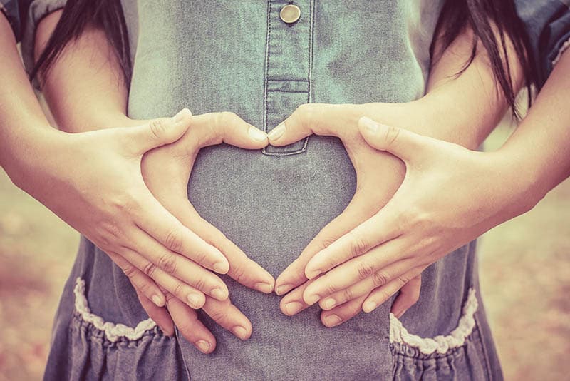 pregnant woman with husband holding hands on belly in heart shape
