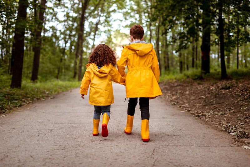 sisters in yellow raincoats holding hands and walking in the wood