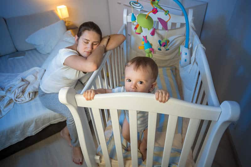 sleepless mother with baby in crib at night