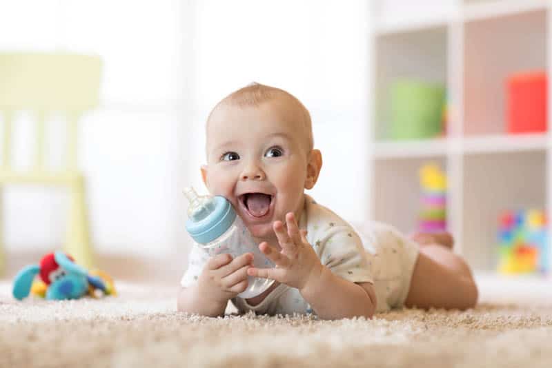 smiling baby with bottle on the floor laying