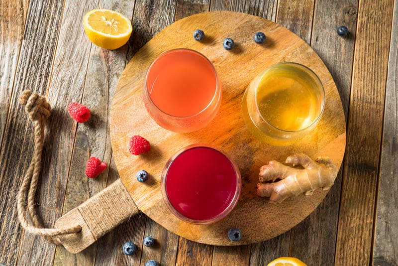 three glass of kombucha with fruits on the wooden board