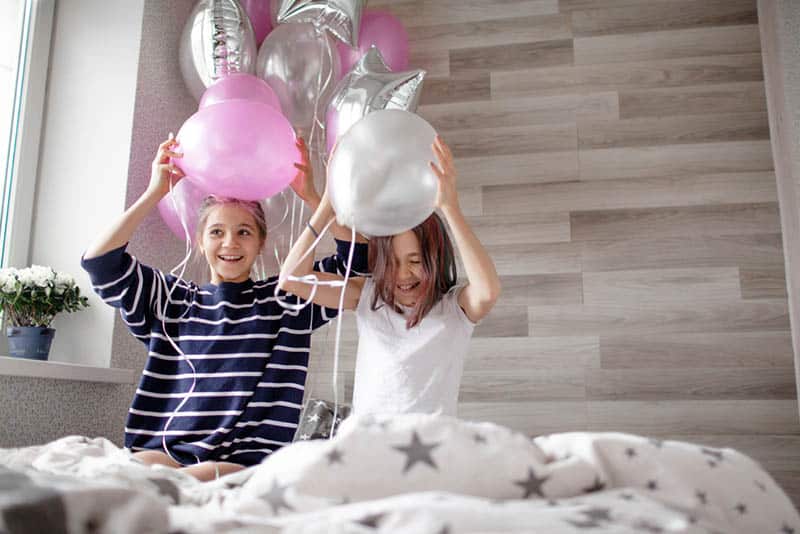 twin sisters playing with birthday balloons on the bed