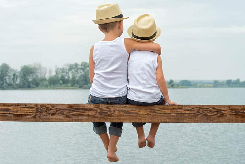 two brothers with hats sitting on the wood in front of the sea