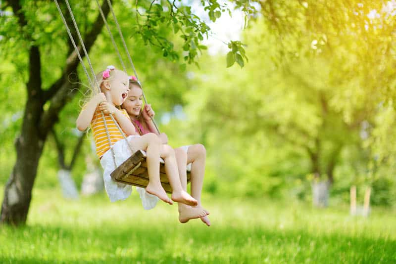two cute sisters swinging together on the swingset in the park