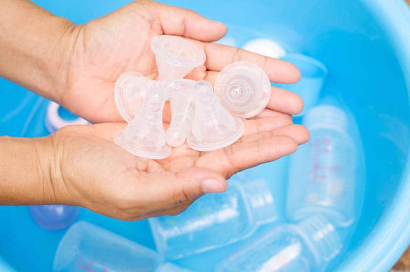 woman holding bottle nipples above the bottles in water