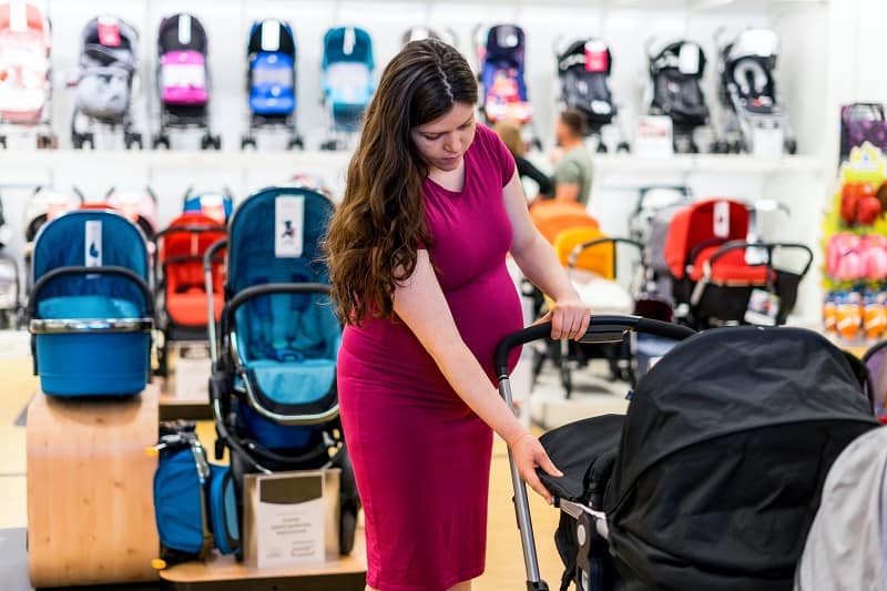 pregnant woman testing out a baby stroller's portability in a baby store