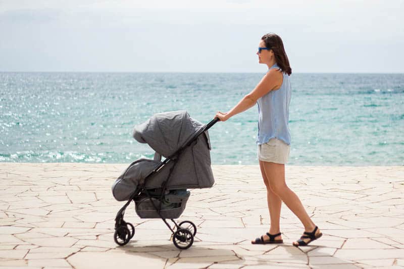 young mother walking with her baby in a stroller by the sea