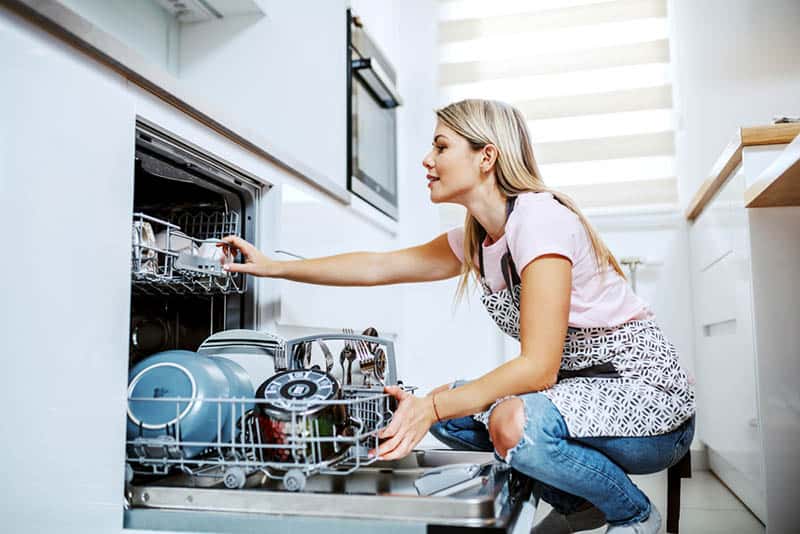 young woman pulling out dishes in a dishwasher