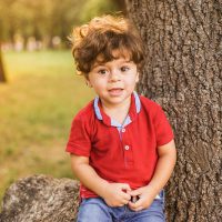 little boy sitting by a tree and posing for a photo