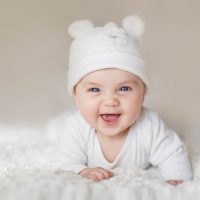 smiling baby wearing a hat with fuzzy ears on the bed