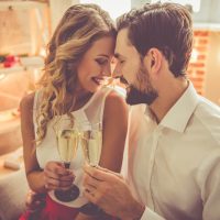 Beautiful young couple is holding glasses of champagne and smiling while celebrating at home
