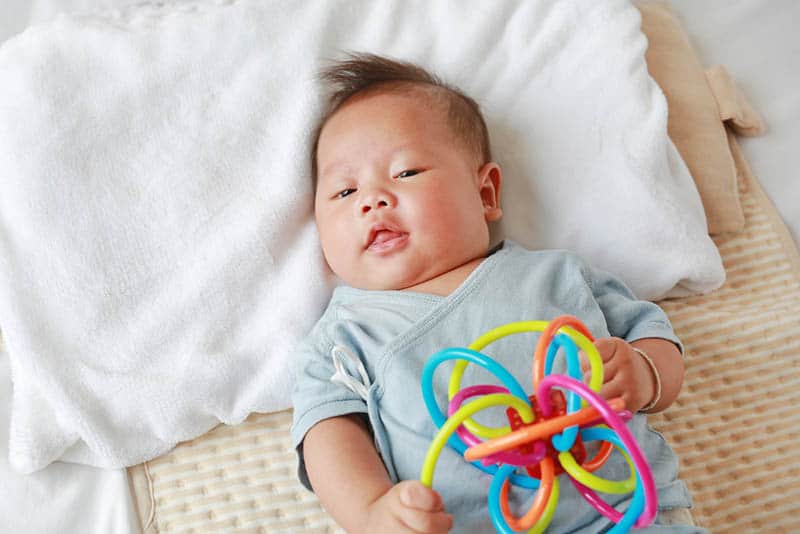 Adorable infant baby boy lying on the bed holding colorful toy
