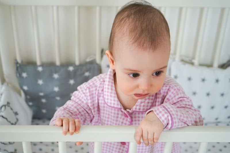 Baby in pink pajamas standing in crib 