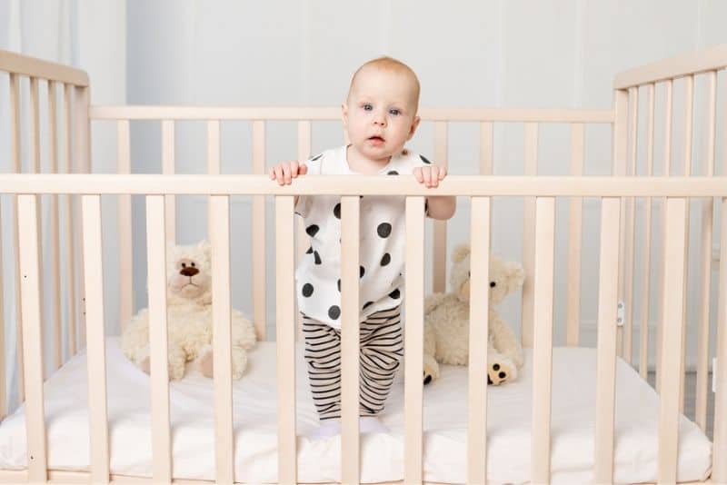 Baby in pajamas standing in crib and holding onto the rails