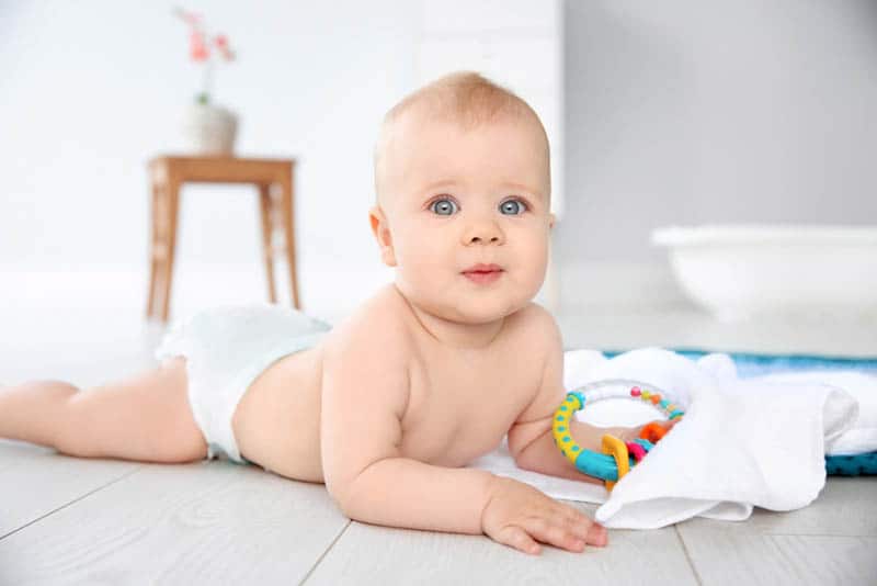 Cute little baby with rattle on floor in bathroom