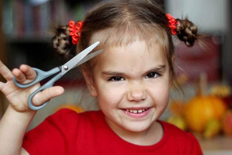 Cute little girl cutting hair to herself with scissors