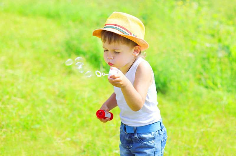 Little boy child blowing soap bubbles outdoors in sunny day