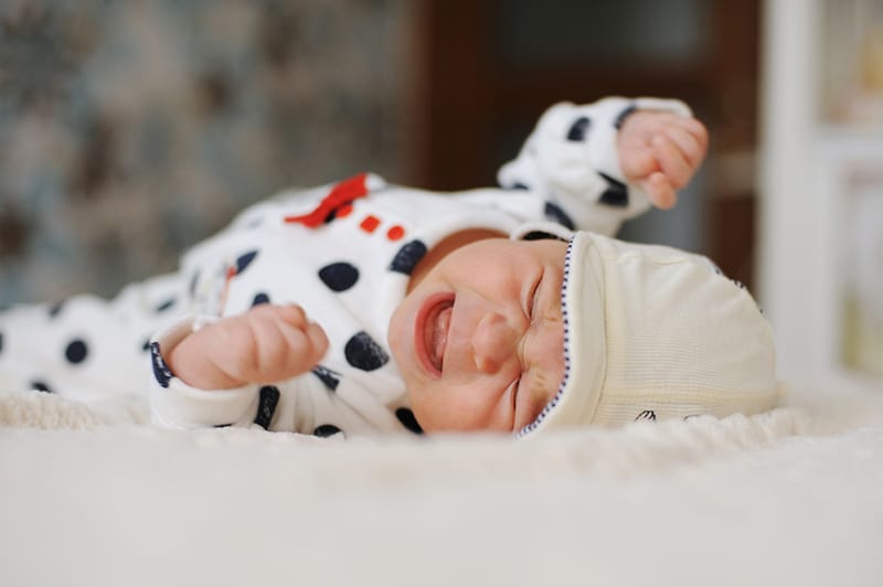 a newborn baby in sweet pijama crying on the bed