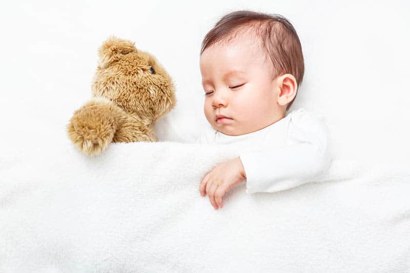 adorable baby boy sleeping in bed with teddy bear