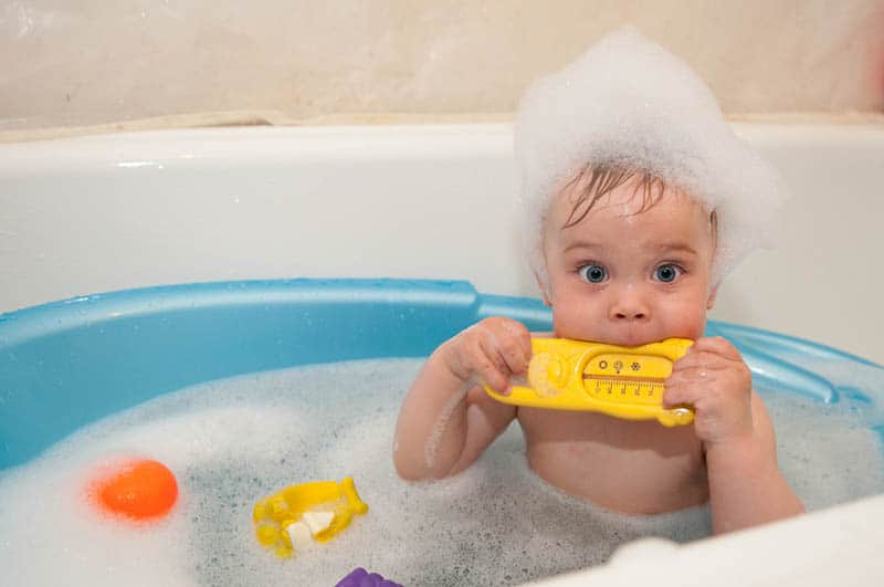 adorable baby boy taking a bath covered with bubble foam and biting a toy