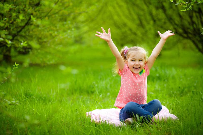 adorable little girl raising hands outdoor in the park