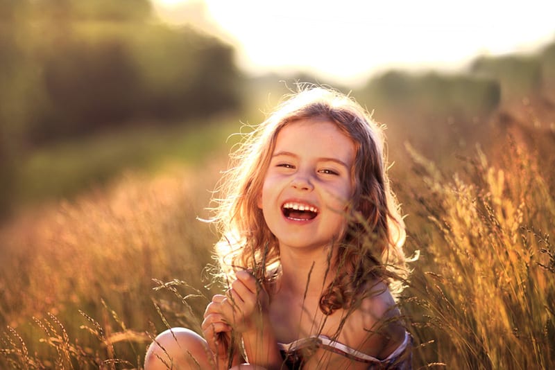 adorable little girl sitting in a meadow and smiling a lot