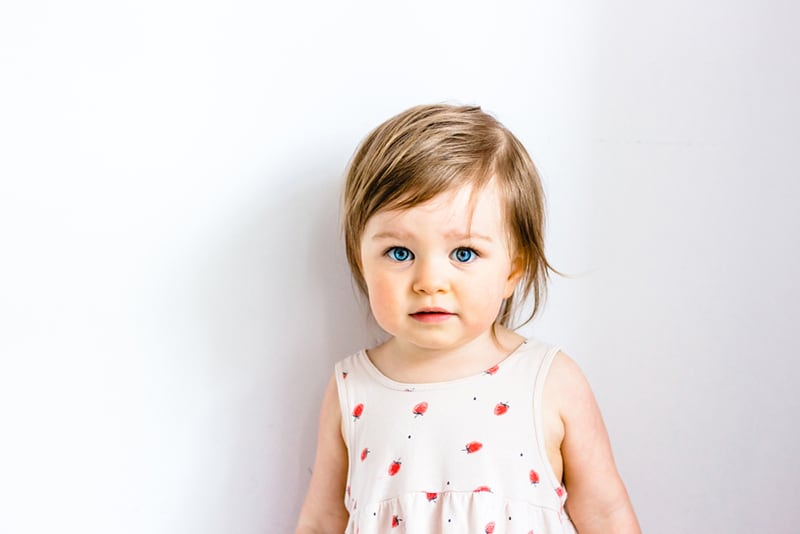 adorable little girl with short hair posing in front of white wall