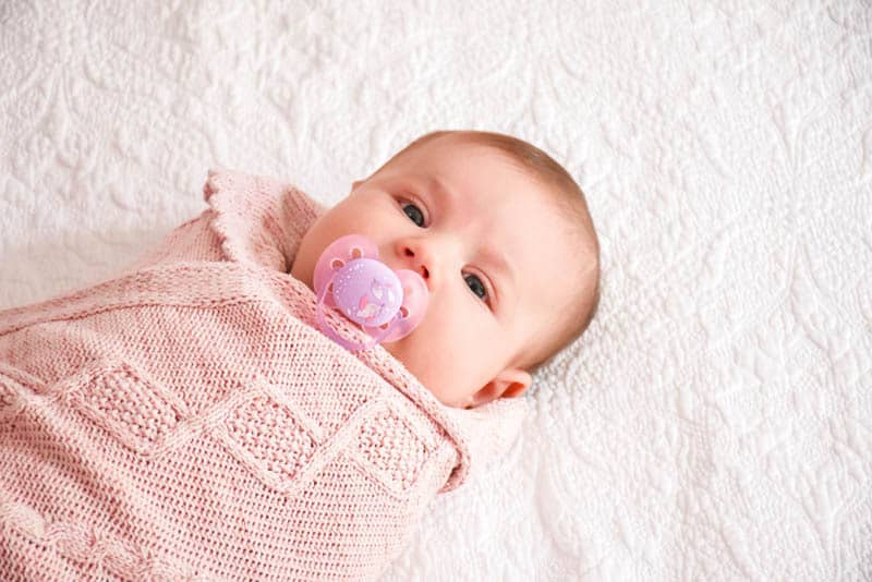 baby girl swaddled in pink cloth with pacifier in mouth