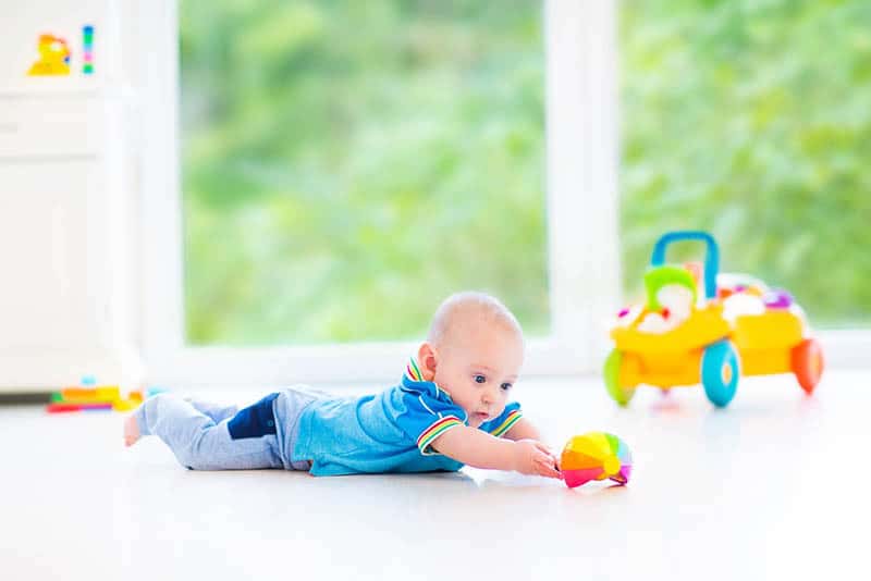 cute baby boy lying on tummy on the floor and playing with toy