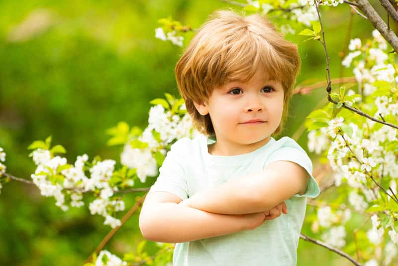 cute little boy standing with crossed arms in nature