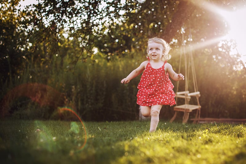 cute little girl in a red dress running in sunlight on the grass