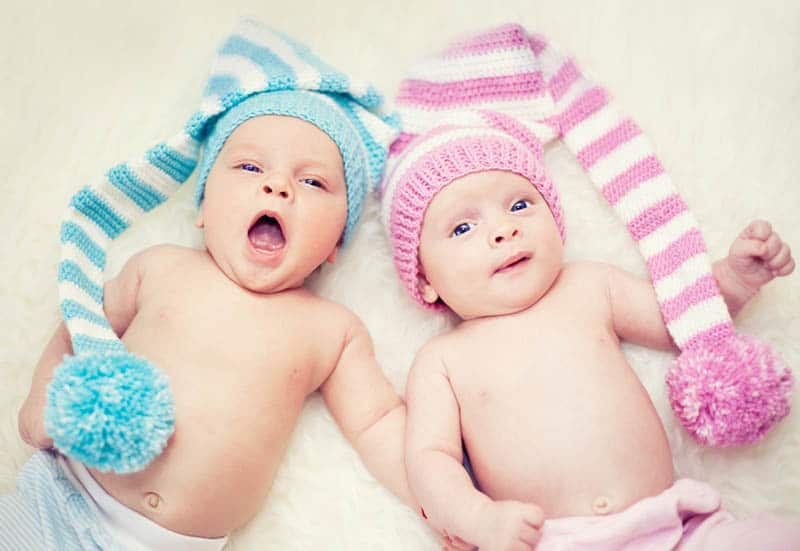 cute twin brother and sister with colorful knitted hats lying on the bed