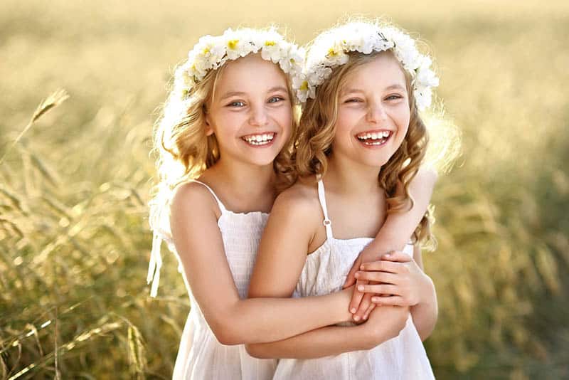 happy twin sisters with flower headband hugging in the field