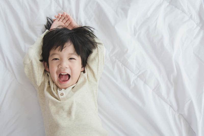laughing little boy lying on back in the bed