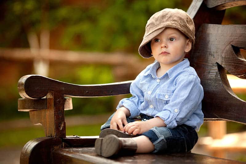 little boy wearing big hat sitting on the bench in the park