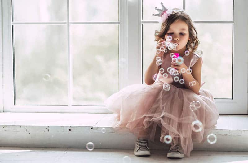 little girl dressed up as a princess blowing soap bubbles