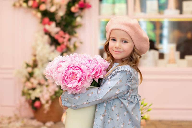 little girl with curly hair and in a beret with bouquet of peonies