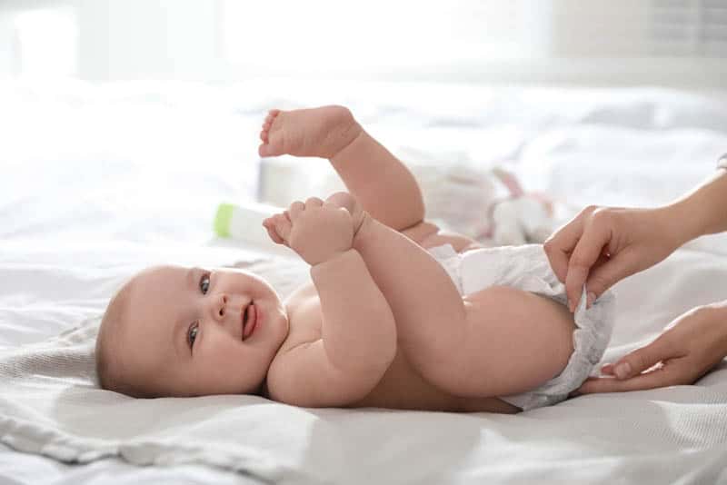 mother changing cute baby diaper on the bed