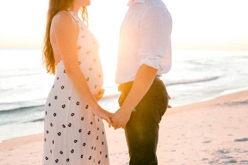 pregnant woman holding hands with her husband on the beach